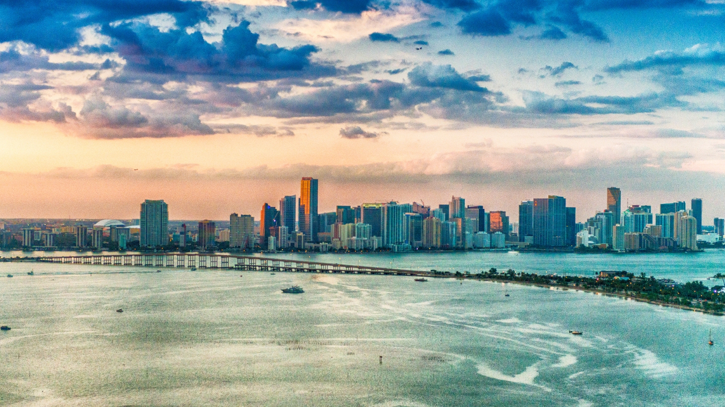 Aerial view of Miami's iconic skyline at sunset, showcasing vibrant colors and a calm waterfront.