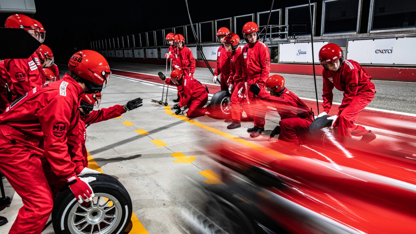 Pit crew in red uniforms executing a high-speed tire change during a Formula 1 race at night.