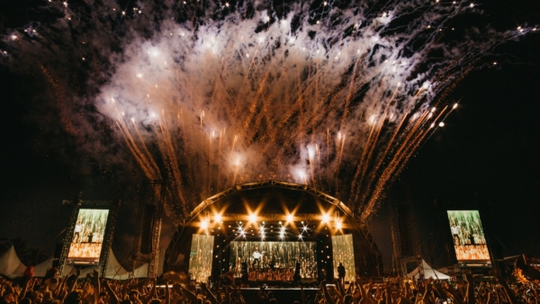 Spectacular fireworks lighting up the night sky during a music festival with a vibrant crowd in the foreground.