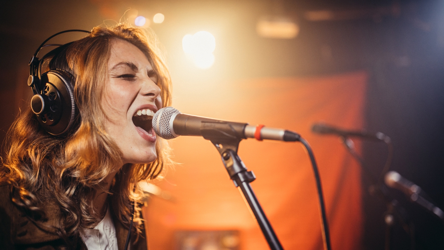 A female artist passionately singing into a microphone during a live performance, showcasing her vocal talent under dramatic lighting.