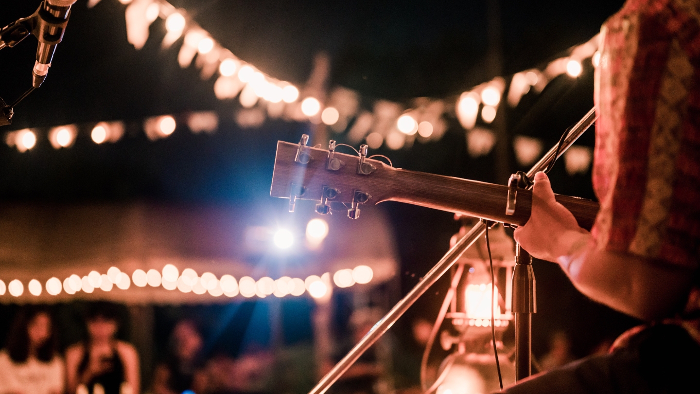 Close-up of an acoustic guitar player performing at an intimate outdoor venue, adorned with glowing string lights at night.