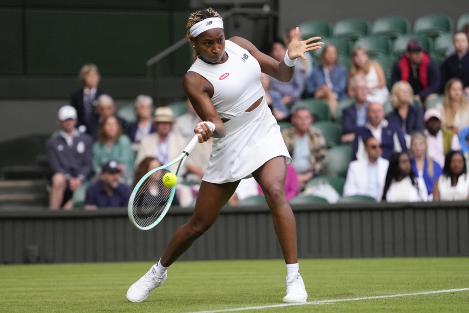 Coco Gauff in action at Wimbledon, wearing a white tennis outfit and hitting a forehand shot during a match on the famous grass courts.