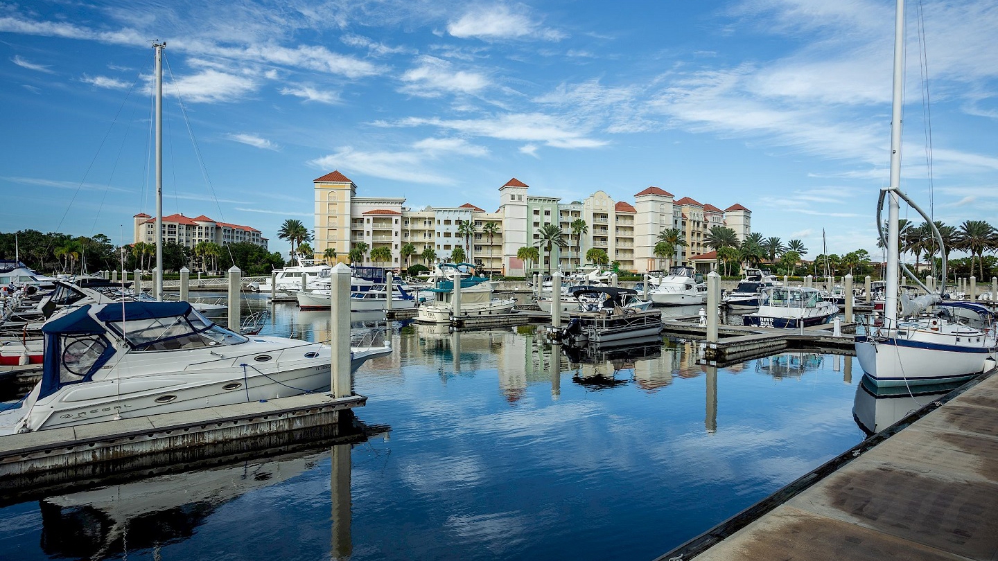 The marina at Hammock Beach Golf Resort, lined with yachts and picturesque views of resort buildings against a blue sky.