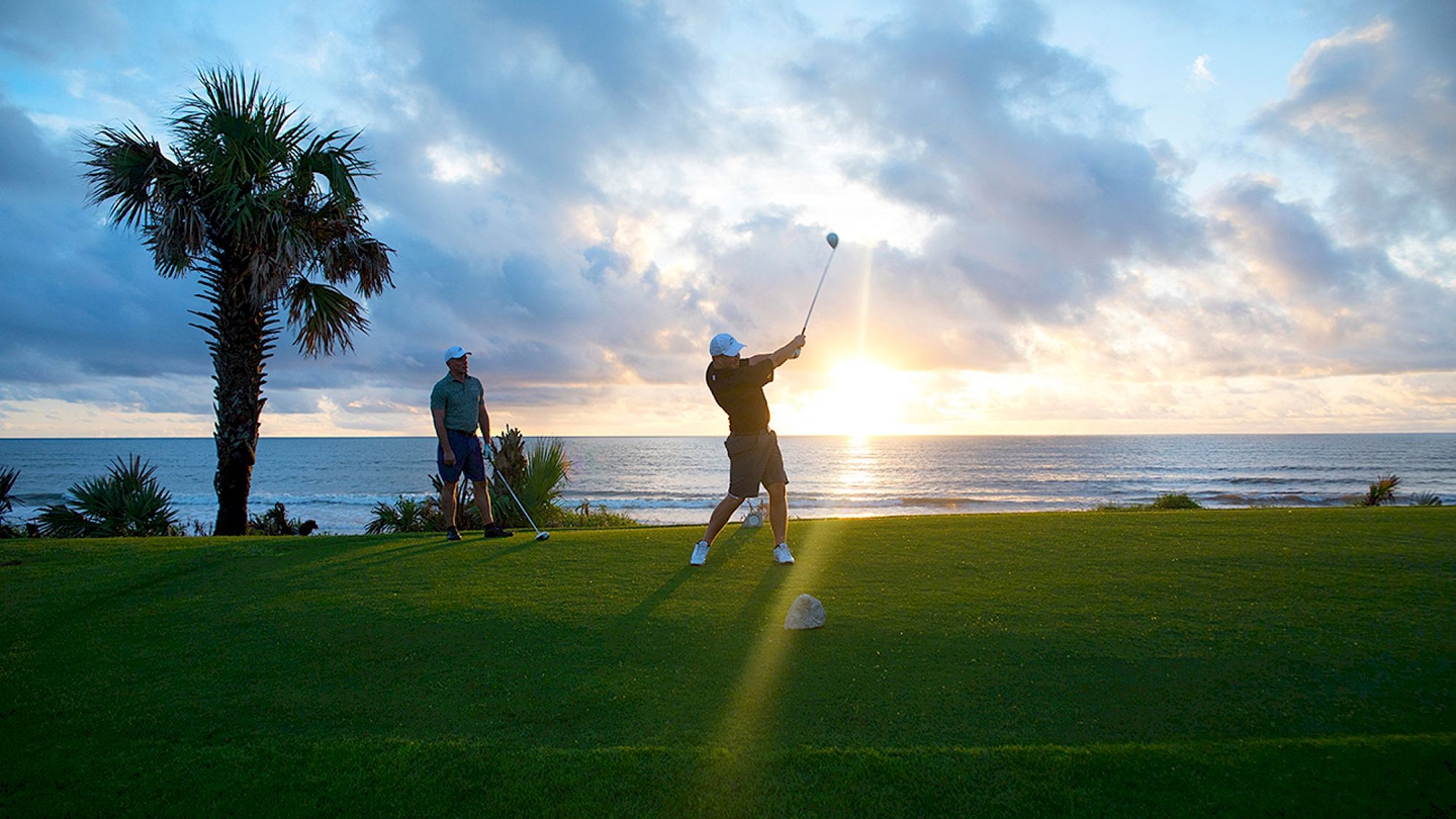 Golfers enjoying a scenic sunrise game at Hammock Beach Golf Resort, with the ocean as a stunning backdrop.