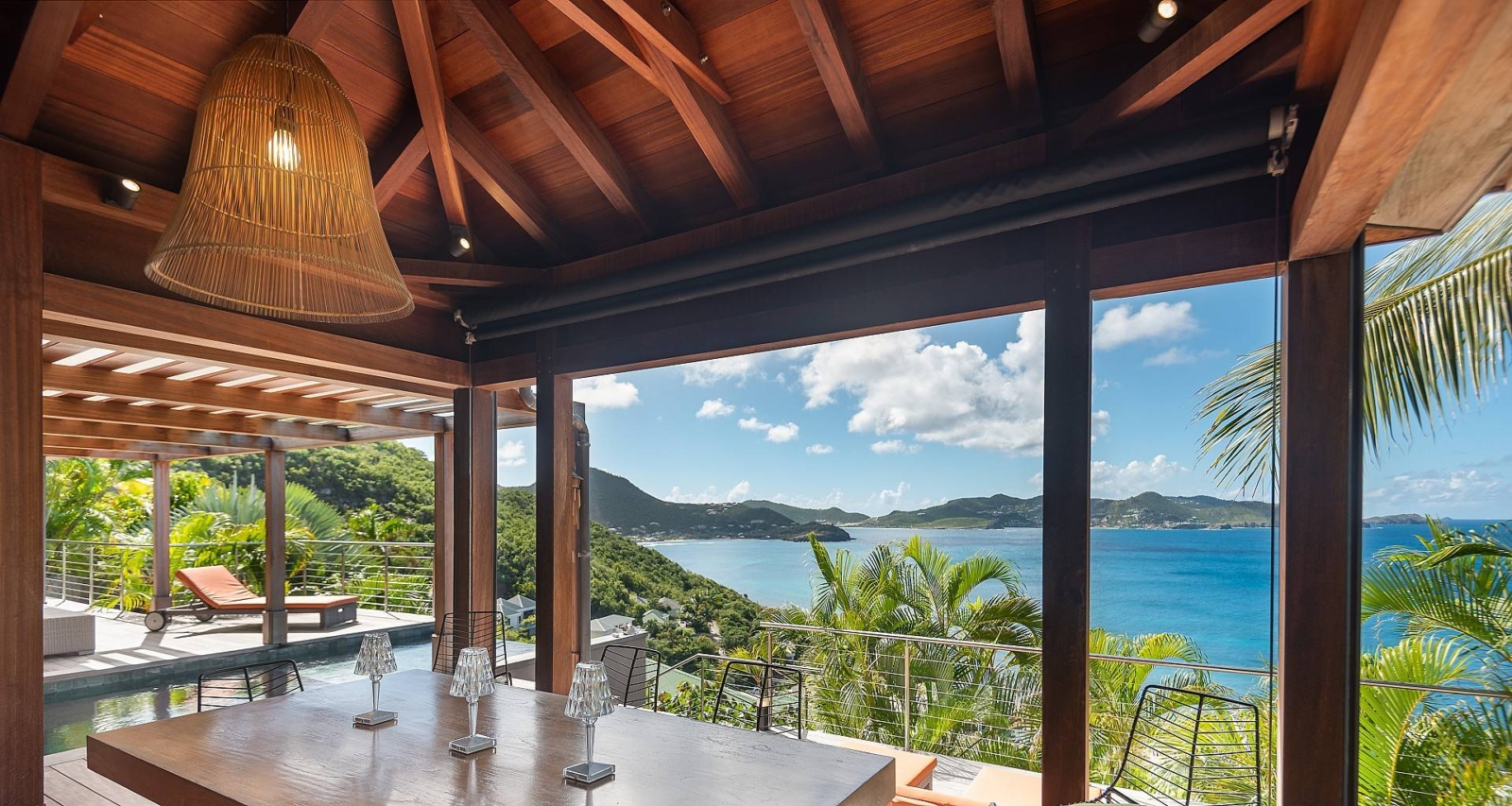 Tropical Dining with Panoramic Views – A beautifully set dining table under a wooden pergola, offering a spectacular view of the ocean and lush hillside, perfect for a St. Barths luxury retreat.