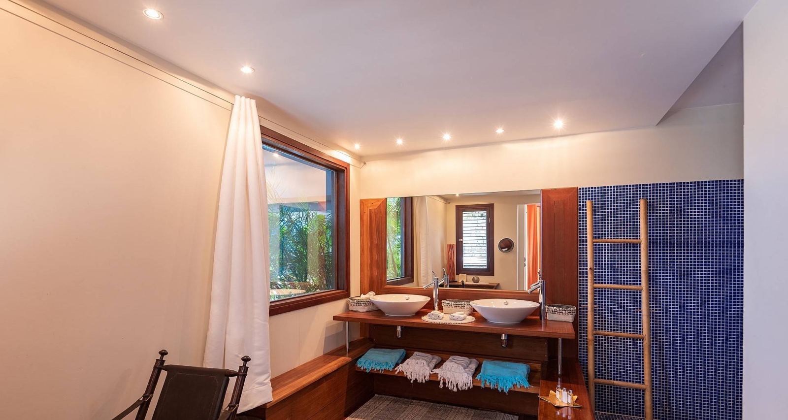 Stylish en-suite bathroom with a modern vanity, bamboo ladder towel rack, and open window inviting natural light and tropical scenery.