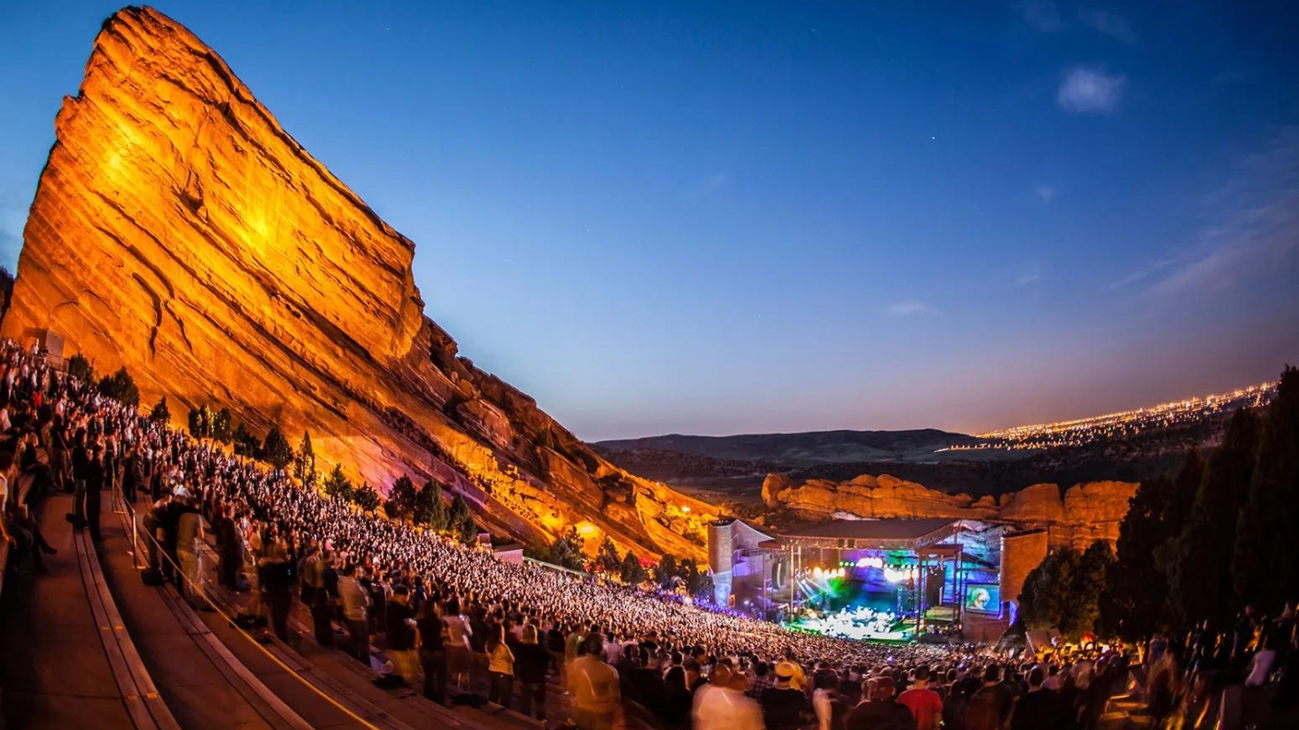 Red Rocks Amphitheatre illuminated at night with a lively crowd enjoying a concert under the starry sky.