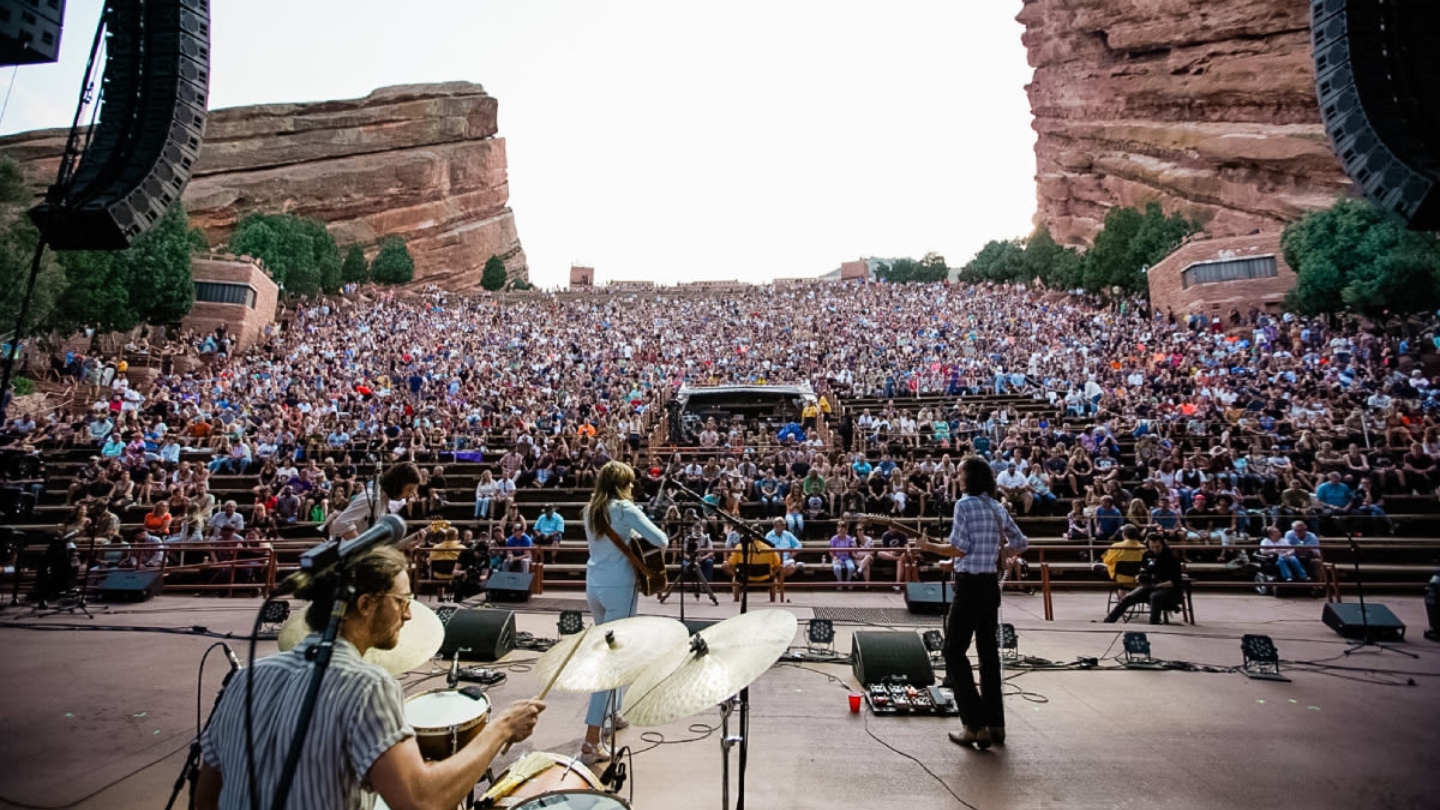 A live band performing in front of a packed audience at the iconic Red Rocks Amphitheatre in Colorado.