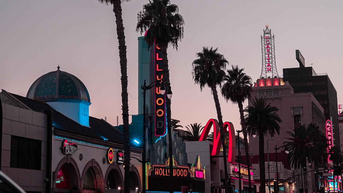 Iconic Hollywood Boulevard at dusk with neon signs and palm trees, featuring the classic California vibe.