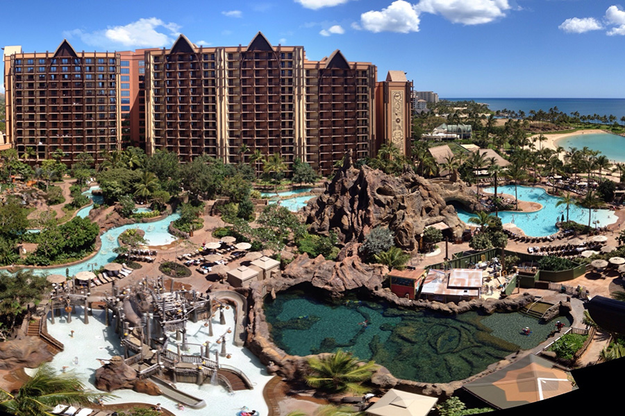 A sweeping aerial view of Aulani’s pools and water playgrounds, surrounded by lush greenery and overlooking the stunning ocean.