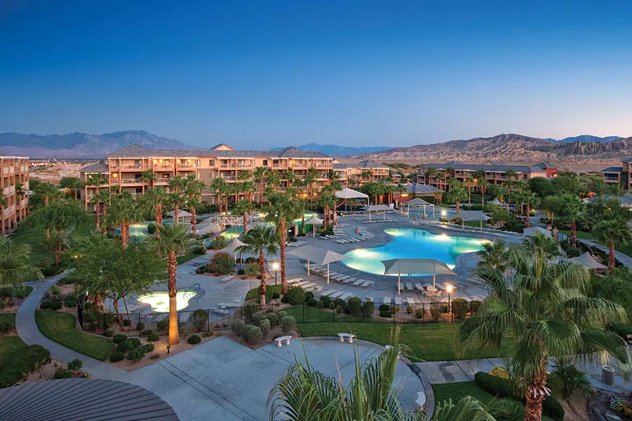 Stunning resort with illuminated pools surrounded by lush palm trees and desert mountains in the background, offering a serene escape for a luxurious vacation experience.