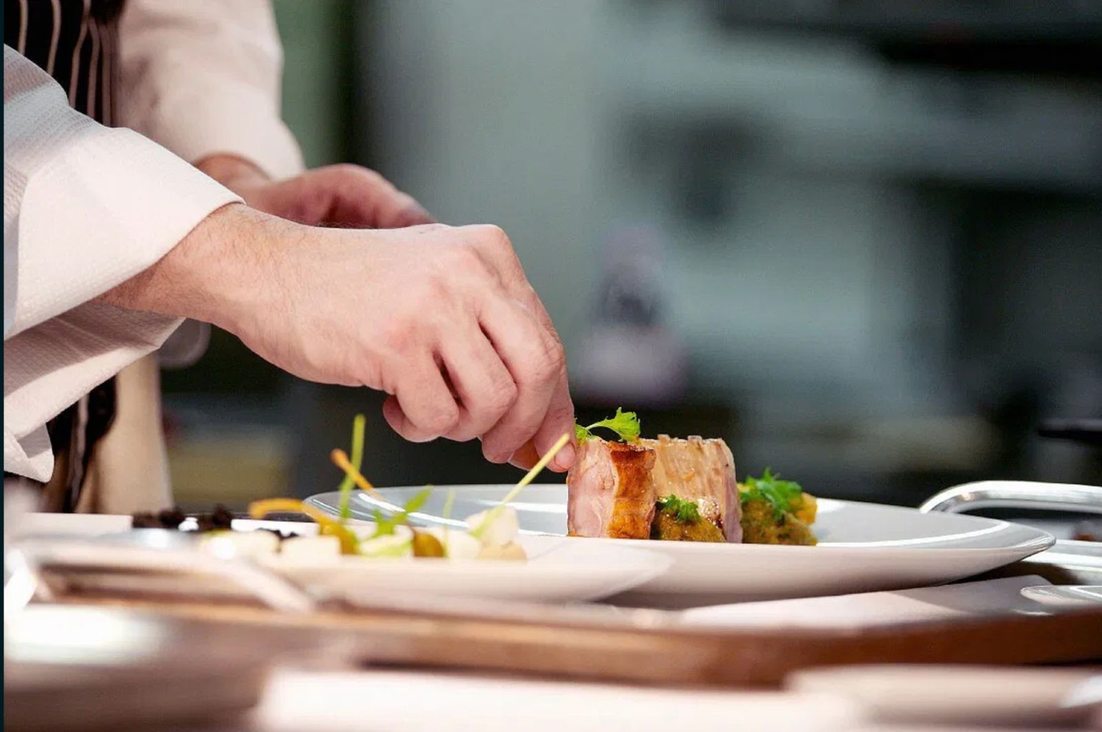 A close-up of a chef’s hands carefully plating a beautifully garnished gourmet dish on a white plate in a fine-dining kitchen