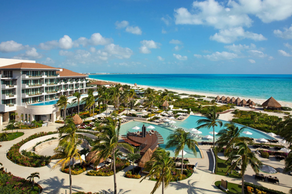 Panoramic aerial view of Dreams Playa Mujeres, featuring elegant beachfront buildings, lush landscaping, and vibrant blue waters.