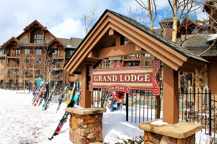 Grand Lodge on Peak 7 entrance sign with skis and snowboards, set against a snowy backdrop in Breckenridge, Colorado.