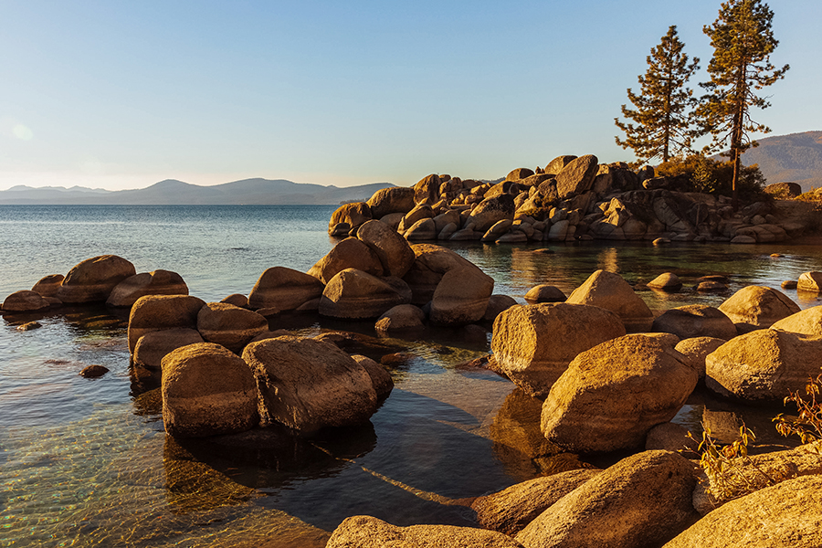 Golden-hour view of Sand Harbor, Lake Tahoe, with smooth rock formations and calm, reflective water.