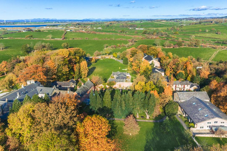 Charming countryside estate surrounded by vibrant autumn foliage, rolling green fields, and historic stone buildings, offering a serene and picturesque retreat in the heart of nature.